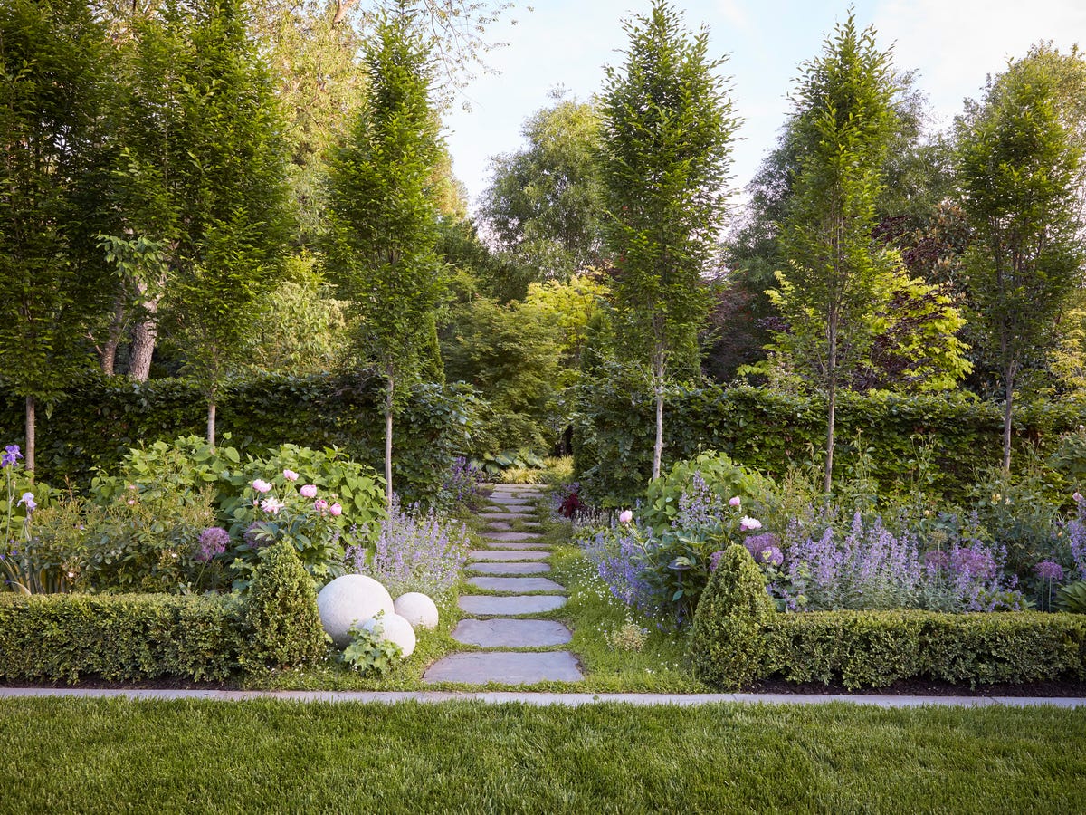 A curved front walkway bordered by a structured perennial bed with repeated clumps and a crisp edging line