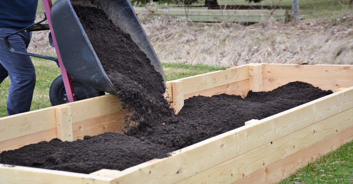 A gardener mixing compost into a front yard garden bed with a shovel next to the house foundation