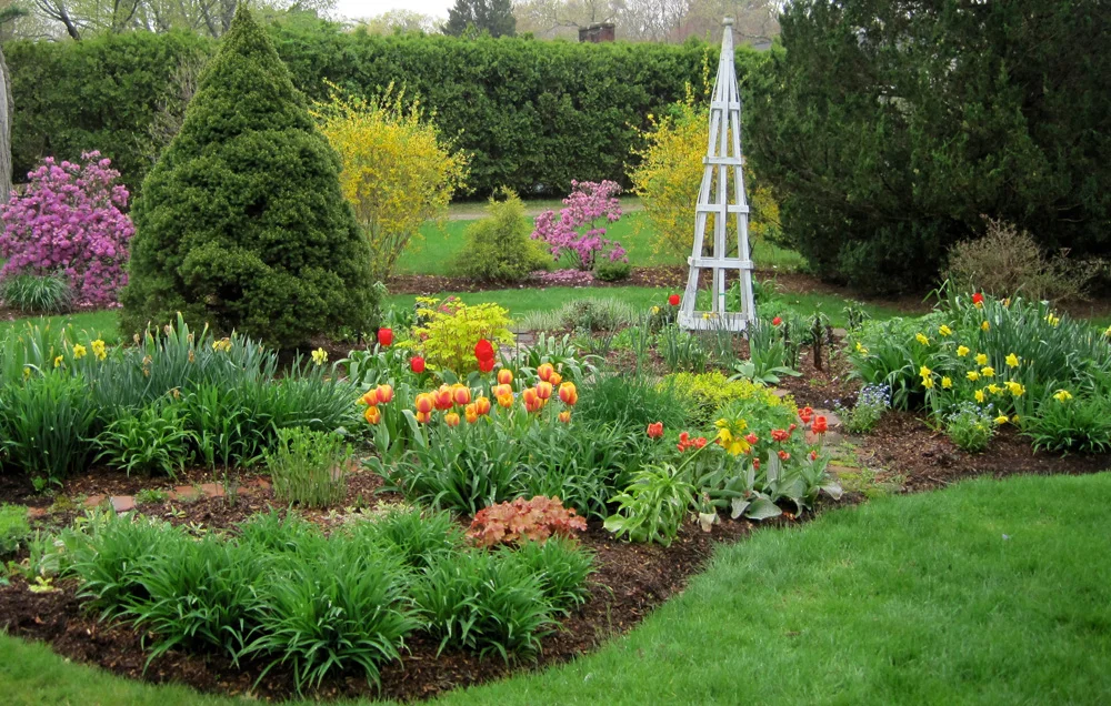 A layered perennial island bed showing taller flowers toward the center, a full mid-layer of blooms, and low edging plants along a clean bed edge
